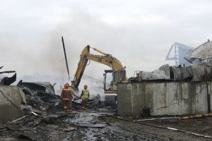 Mike Peterson operates an excavator Sunday morning while firefighters douse flames. The excavator was brought in as part of an effort to get at a hot spot. -- Tim Engstrom/Albert Lea Tribune