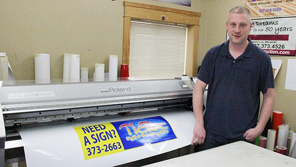 Nick Rogness poses for a photo next to Tic Toc Digital Printing’s printer as it finishes up a decal. --Kelli Lageson/Albert Lea Tribune
