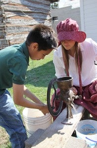 Mario Guerra, a fifth-grader from St. Theodore Catholic School, tries his hand Tuesday at grinding corn as 11th-grader Anna Anderson watches. Albert Lea High School juniors taught local fifth-graders about early pioneer times during Discover History Days at the Freeborn County Historical Museum.