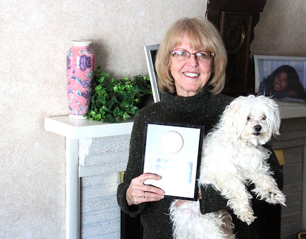 Vikki Pence stands in her living room holding her dog Harley and the Breaking Barriers Award she received earlier this month. -- Drew Claussen/Albert Lea Tribune 