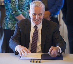 Gov. Mark Dayton signs a bill June 13 at Edgewater Bay Pavilion for the state dedicating $7.5 million from the 2014 construction bill to the $15 million dredging of Fountain Lake. – Colleen Harrison/Albert Lea Tribune