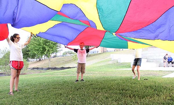 Children play under a parachute with Albert Lea Parks and Recreation staff Tuesday during a rededication of the park. – Sarah Stultz/Albert Lea Tribune