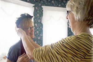 Su Evans, right, ties a vintage bonnet on to Bonnie Rodberg. Vintage clothing is displayed throughout the Victorian house in Lake Mills. – Hannah Dillon/Albert Lea Tribune