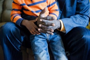 Dabang Gach's son Keat Ruot, 5, holds his father's hands as Gach recounts what life was like in South Sudan before coming to the U.S. as a refugee. -- Colleen Harrison/Albert Lea Tribune