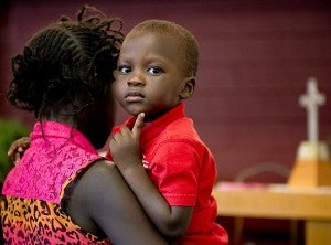 Sudanese children, especially those in the Nuer tribe, are generally raised to be independent and self-sufficient. It’s common for children to help take care of their younger siblings, like the girl pictured is taking care of her younger brother during a Sudanese worship service. – Colleen Harrison/Albert Lea Tribune