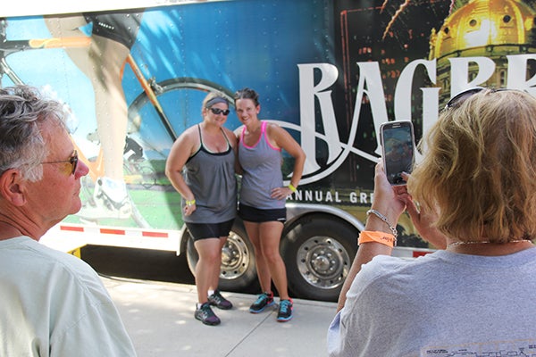 Mother Jan Hanold takes a photo of daughters Alison Hanold and Stephanie Anacker beside an official RAGBRAI trailer while father John Hanold watches Wednesday in Mason City. The family was from Wisconsin. — Tim Engstrom/Albert Lea Tribune