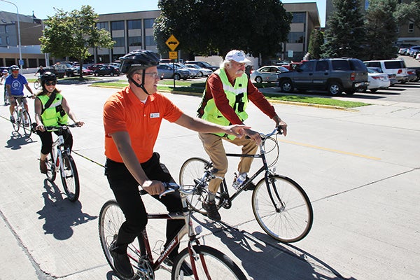 Albert Lea City Manager Chad Adams, in orange, points while riding a bicycle with transportation infrastructure expert Dan Burden. – Tim Engstrom/Albert Lea Tribune
