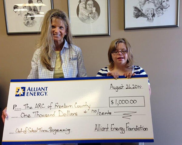 Rebecca Gisel of Alliant Energy awards Becca Schei a check for $1,000 for the Out-of-School programs at the Arc of Freeborn County. – Provided