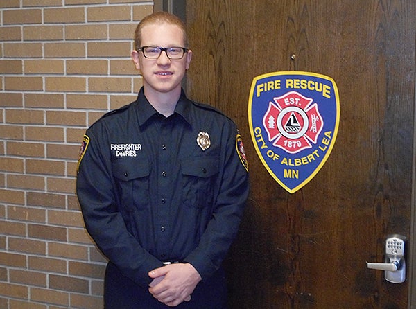 Albert Lea firefighter Jordan DeVries stands in the new uniforms of the Albert Lea Fire Department next to an image of the new patch for the department on the door of the Fire Department living quarters at City Hall. - Provided
