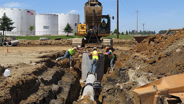 Workers lower a sewage pipe into the ground near the intersection of highways 14 and 42, just outside the southeastern Minnesota town of Eyota on June 9. It's the site of the state's newest roundabout. — Elizabeth Baier/MPR News