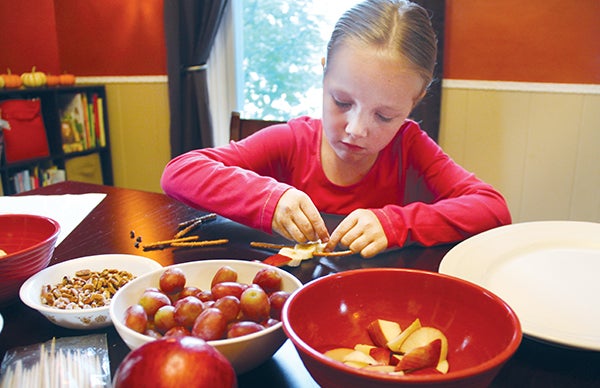 Seven-year-old Sophie Stultz focuses as she puts together a snowman kabob made of bananas, apples, grapes, pretzel sticks, miniature chocolate chips and a walnut piece. 