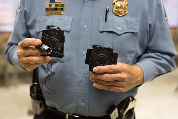 Minneapolis Police Lt. Greg Reinhardt holds up two body cameras at Minneapolis City Hall. The one on the left attaches to the lapel or glasses while the one on the right mounts on an officer’s chest. - Jennifer Simonson/MPR News 