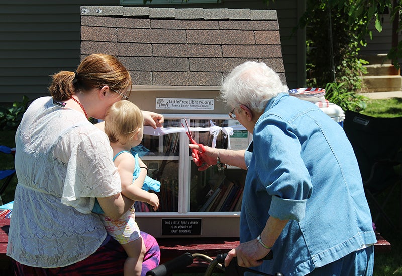 The youngest and the oldest in attendance at the dedication of the Little Free Library cut a ribbon during the ceremony ouside the house. - Sarah Stultz/Albert Lea Tribune