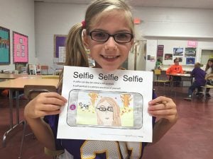 Hawthorne Elementary School fifth-grader Imogene Brumbaugh stands with artwork created during a self-portrait lesson. Provided